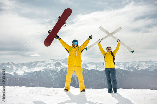 Couple of skier and snowboarder are standing at mountain top, holding ski and snowboard in hands and having fun. Winter sports at ski resort concept