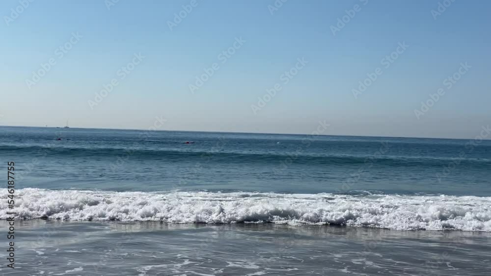 wide view of small waves at Torre beach with some swimmers training in the background in Cascais, Portugal wide view of small waves at Torre beach with some swimmers training in the background in Cascais, Portugal