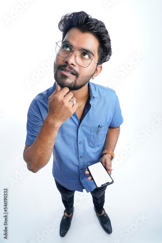 Young indian man using smart phone standing over isolated white background serious face thinking about question or solution, very confused idea