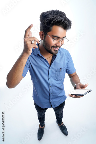 Young indian man using smart phone standing over isolated white background serious face thinking about question or solution, very confused idea
