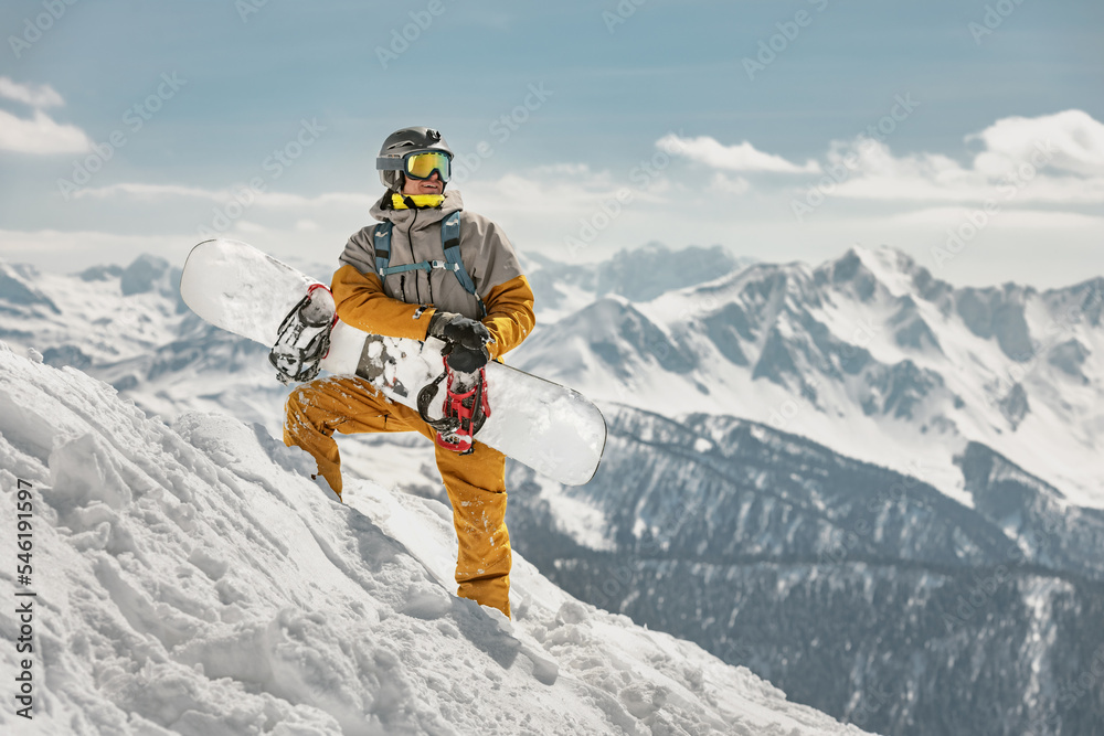 Handsome male snowboarder stands at ski slope with snowboard in hands. Ski resort concept