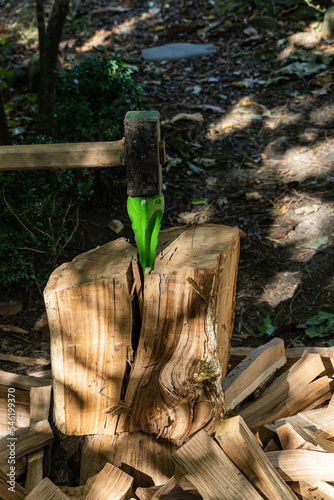 Splitting problematic oak stumps with metal wedge and sledgehammer. Close-up. Wedge sticks out of deep crack in stump. Blurred background. Selective focus. Preparing firewood for  stove or fireplace. photo