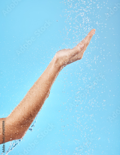 Hand, shower and water for skincare hygiene, wash or dermatology against a blue studio background. Arm and hands of person in healthy wellness, skin hydration and washing for body care treatment