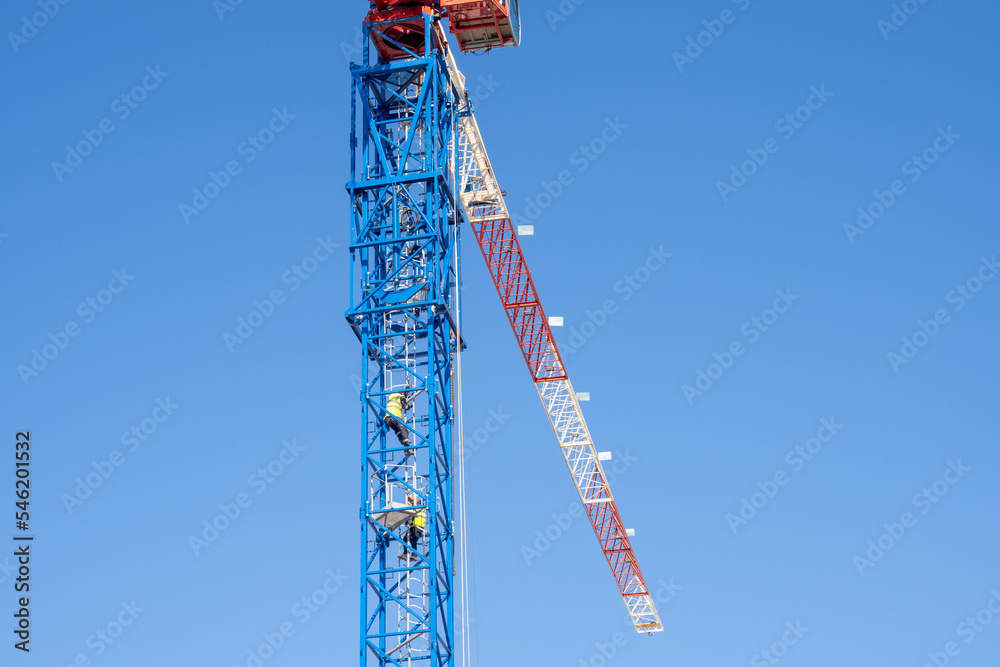 Workers climb the tower crane. The crane operator climbs the metal ladder to the workplace. Builders mount a crane at a construction site. Workers climb the tower crane. The crane operator climbs the metal ladder to the workplace. Builders mount a crane at a construction site.