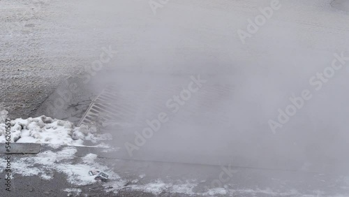 Steam is coming from the storm sewer on the road. Cold winter weather, snowfall