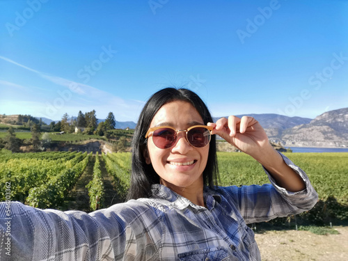 Selfie of a young Asian woman at vineyards landscape in Naramata, Okanagan valley, British Columbia, Canada. Canadian agriculture eco tourism concept.