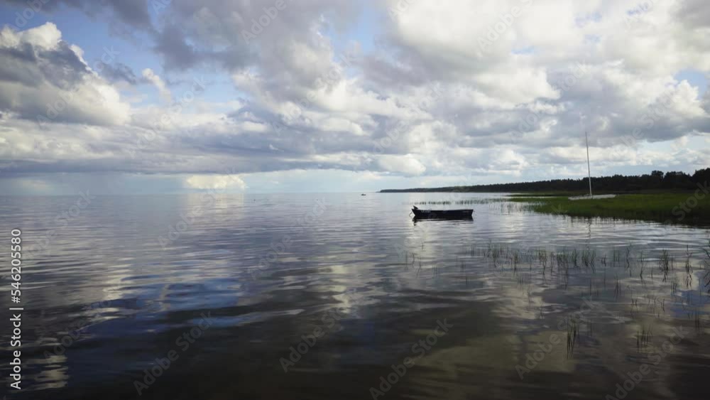A fishing boat sways on the waves of the baltic on a summer day. Green grass in the water against the background of clouds on the horizon. The sky is reflected in the water. Latvia A fishing boat sways on the waves of the baltic on a summer day. Green grass in the water against the background of clouds on the horizon. The sky is reflected in the water. Latvia