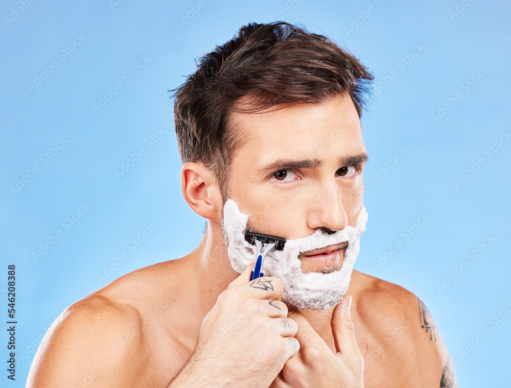 Man, razor and shaving for haircare, grooming and hair removal for hygiene on a blue studio background. Portrait, man and beauty to shave beard or face with foam or soap for facial cleansing