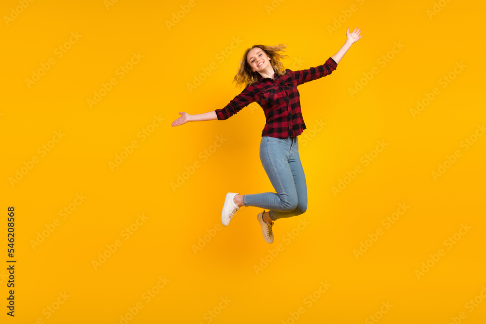 Full length of cheerful wavy-haired girl jumping having fun rising hands isolated on bright vibrant color background
