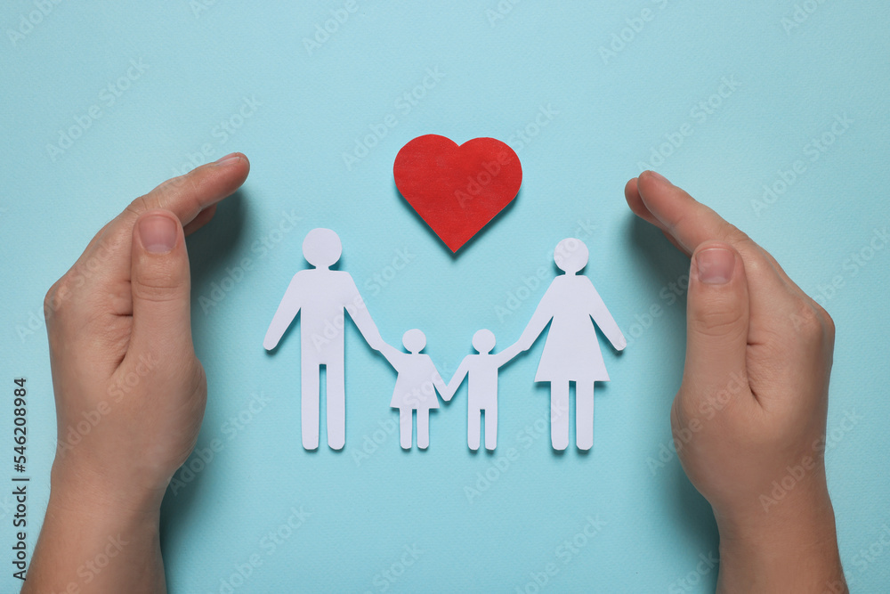 Man protecting paper family figures and red heart on light blue background, top view. Insurance concept Man protecting paper family figures and red heart on light blue background, top view. Insurance concept