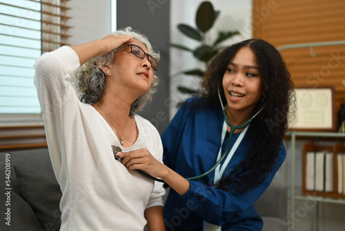 Positive female health visitor examining senior female patient during home care visit. Elderly healthcare concept