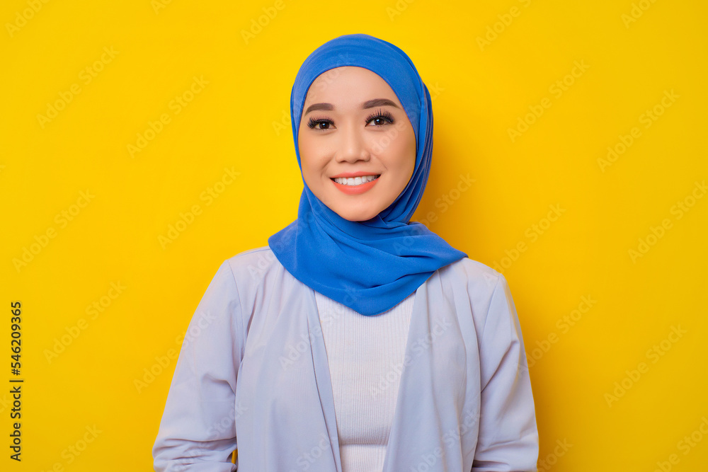 Close-up of smiling young Asian Muslim woman looking at camera isolated over yellow background