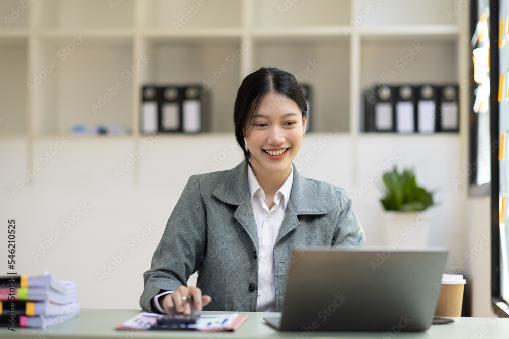 Attractive Asian businesswoman working at her desk, using calculator and laptop Attractive Asian businesswoman working at her desk, using calculator and laptop