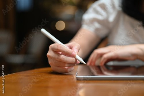 Asian female using stylus pen drawing on her tablet while relaxing in the coffee shop. cropped