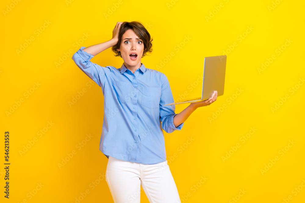 Fototapeta premium Photo of adorable pretty terrified girl with bob hairdo dressed blue shirt hold laptop hand on head isolated on yellow color background