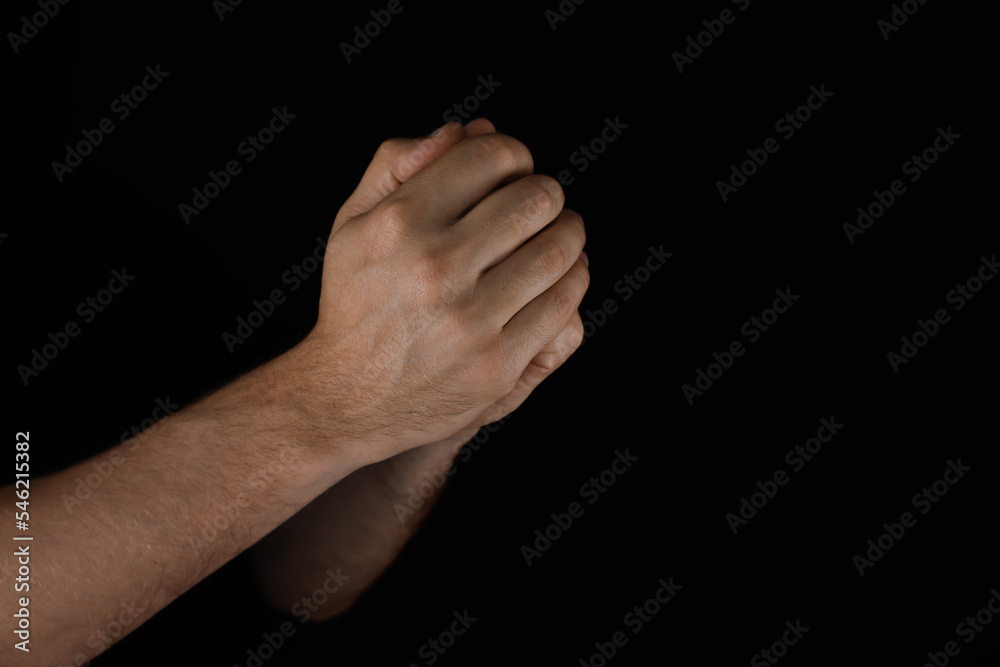 Man praying against black background, closeup view Man praying against black background, closeup view