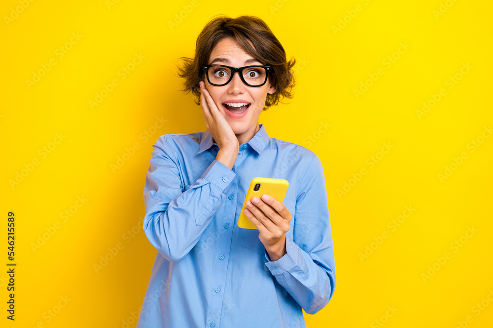 Closeup photo of young attractive funny excited positive surprised woman  touch cheeks hold phone eshopping summer sale isolated on yellow color  background фотография Stock | Adobe Stock