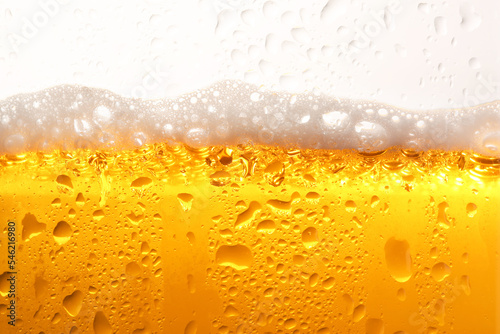 Glass of tasty cold beer with foam and condensation drops on white background, closeup