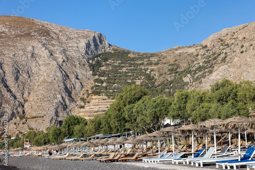 Fototapeta Naklejka Na Ścianę i Meble -  : Sun loungers on the black volcanic beach of Kamari in Santorini. Cyclades, Greece