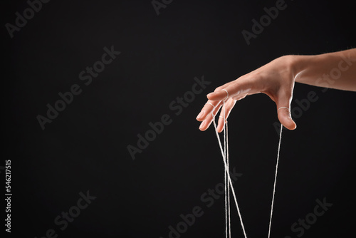 Fototapeta Woman pulling strings of puppet on black background, closeup