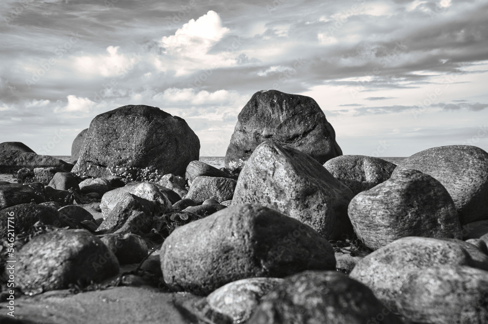 Big stones in black and white taken on stone beach in front of sea with clouds in sky Big stones in black and white taken on stone beach in front of sea with clouds in sky