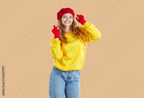 Autumn mood. Cute young woman in autumn casual clothes is having fun on light beige background in studio. heerful girl wearing yellow sweatshirt, jeans, red beret and gloves is dancing and smiling.