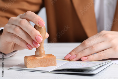 Ukraine, Lviv - September 6, 2022: Woman stamping visa page in passport at white wooden table, closeup photo