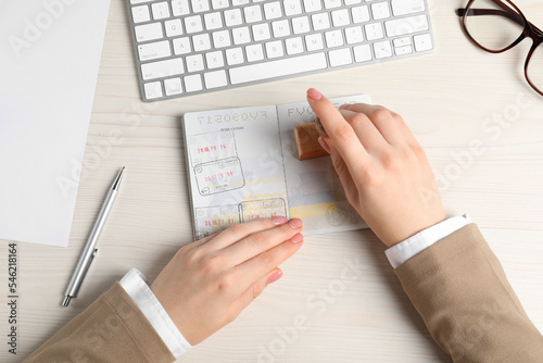 Ukraine, Lviv - September 6, 2022: Woman stamping visa page in passport at white wooden table, top view