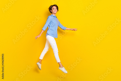 Full length photo of sweet adorable girl dressed blue shirt jumping high walking empty space isolated yellow color background