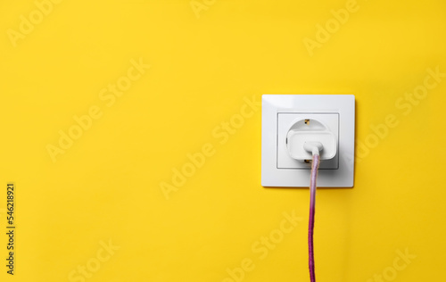 Charger adapter plugged into power socket on yellow wall, space for text. Electrical supply