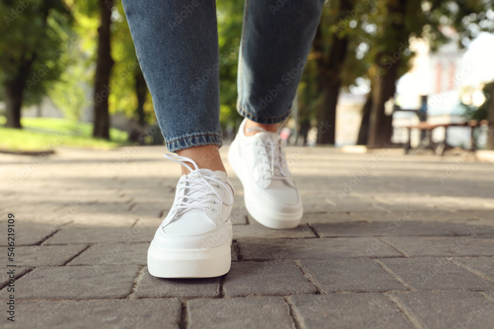 Woman in stylish sneakers walking on city street, closeup