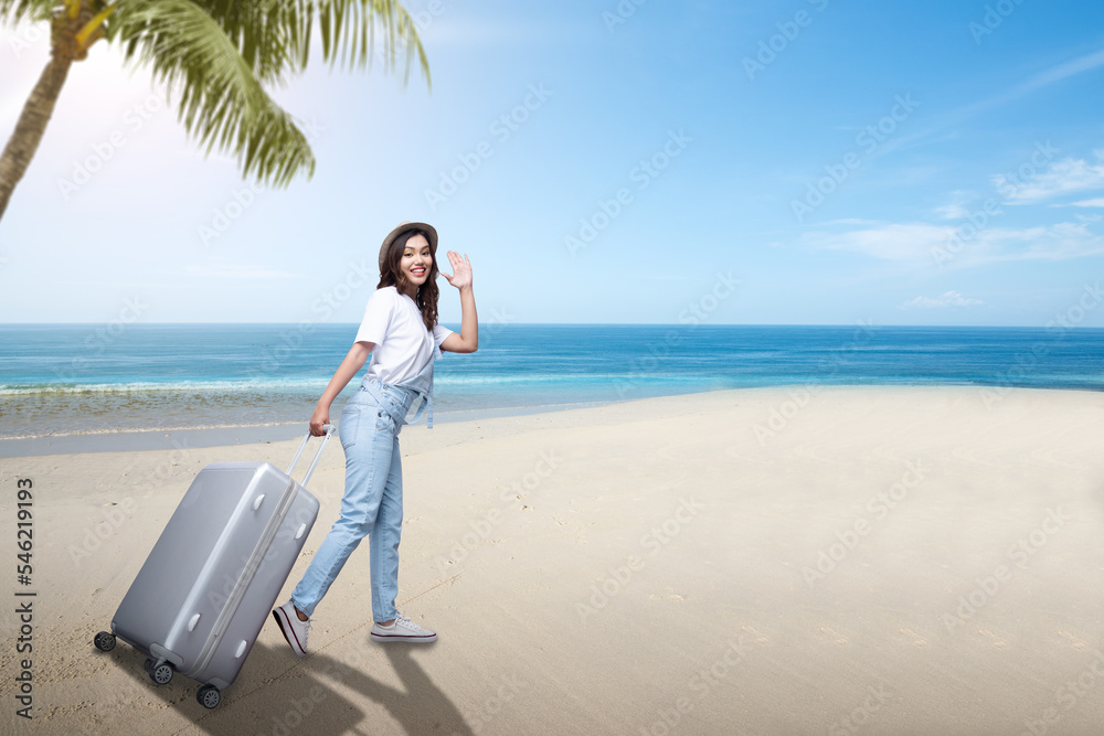 Asian woman with a hat and carrying suitcase on the beach