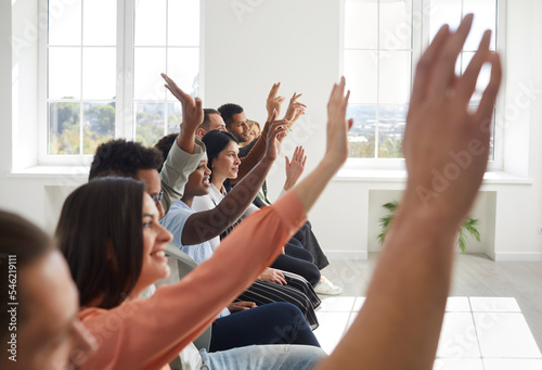 I have question. Group of people sitting on chairs in conference room raise their hands wanting to ask questions. Event for business and entrepreneurship. Selective focus. Blurred front.