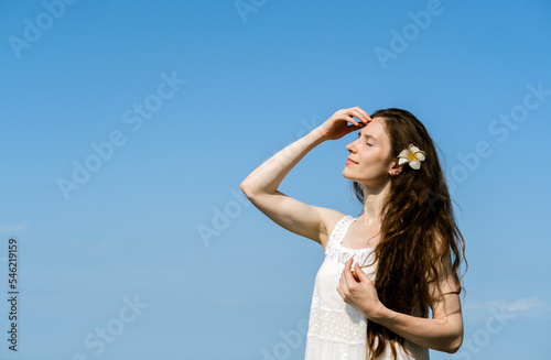 Beautiful young woman with healthy skin and dark long hair enjoying summer hot weather on a background of clear blue sky. Copy space.