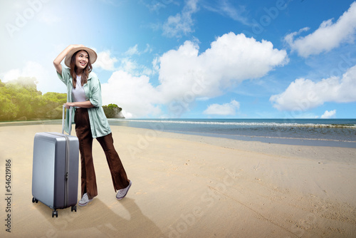 Asian woman with a hat and suitcase standing on the beach