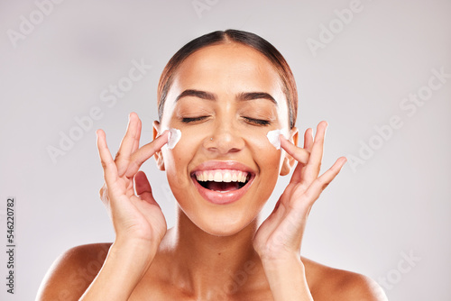 Skincare, beauty and woman with face cream in a studio doing a natural face and skin routine. Cosmetic, wellness and happy girl model with facial lotion, spf or sunscreen isolated by gray background.