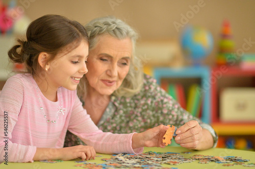 Grandmother with little granddaughter collecting puzzle