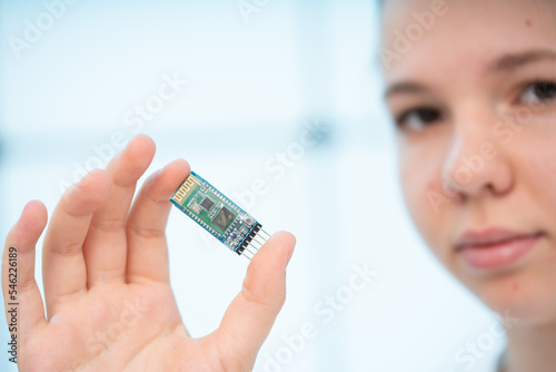 girl holds in her hands a miniature radio transmitter module for exchanging digital information in the smart home system photo