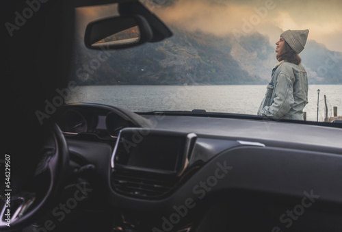 Young woman driver traveler enjoying lake view on foggy autumn day, view through car © olezzo
