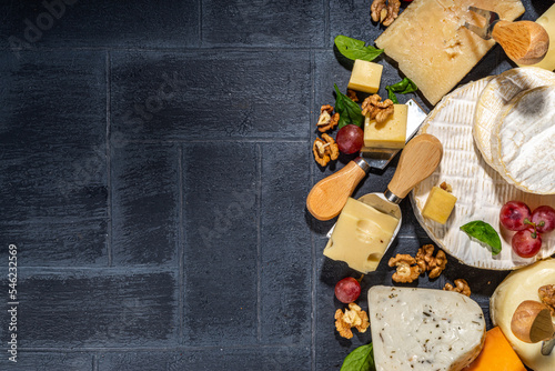 Different sorts of cheese set. Cheese platter with various cheese, with grapes, nuts, cheese knife and spices, black tiled background copy space