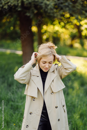 Caucasian blonde woman wearind trench smile happily on sunny spring day outside walking in park photo