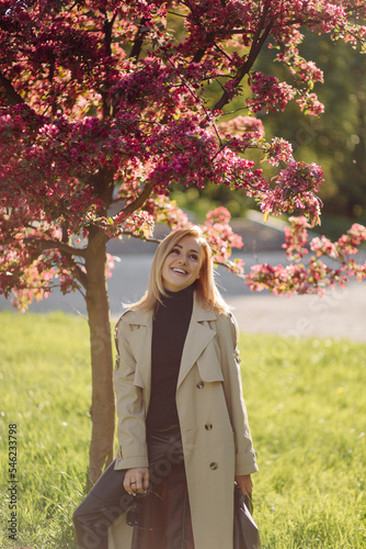 Caucasian blonde woman wearind trench smile happily on sunny spring day outside walking in park photo