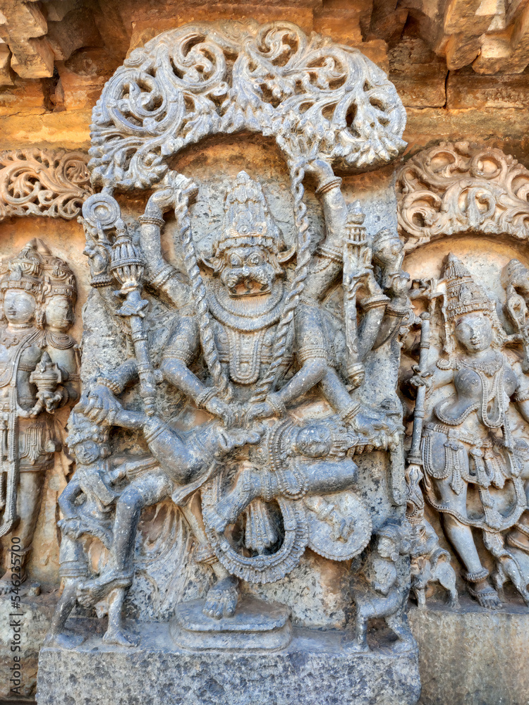 Obraz premium Stunning bas-relief of Ugra Narasimha, an avatar of Vishnu, adorns the Hoysaleswara Temple in Halebidu, India. The carving shows the fierce deity subduing demon king Hiranyakashipu with multiple arms.