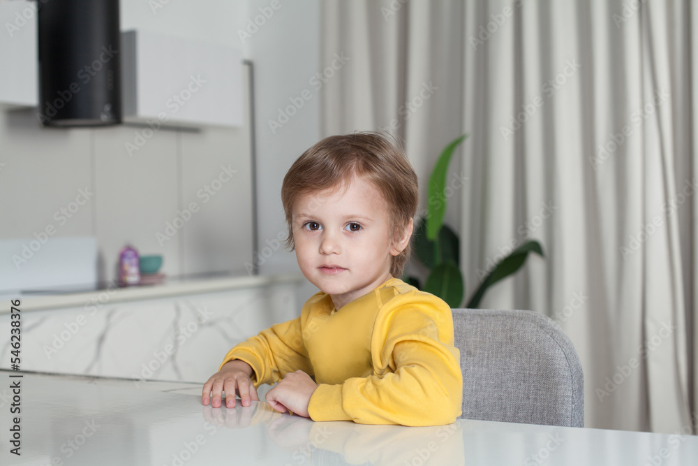 Happy child boy with brown hair in yellow sweater sitting on studio kitchen background Happy child boy with brown hair in yellow sweater sitting on studio kitchen background