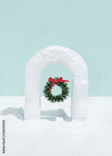 Christmas wreath in snow covered gate on blue background. Minimal creative christmas concept. Upright rectangle layout with copy space.