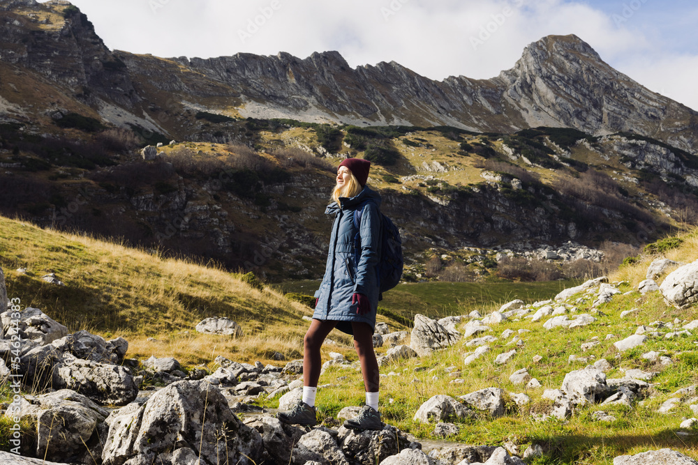 A young woman in a jacket and hat with a backpack while hiking. Beautiful autumn landscape.in the mountains