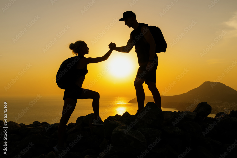 Silhouettes of two people who help each other while climbing mountains in the setting sun