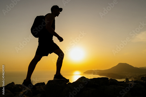 Stunning mountain landscape. The silhouette of a man walking on the rocks of the mountains while hiking at sunset