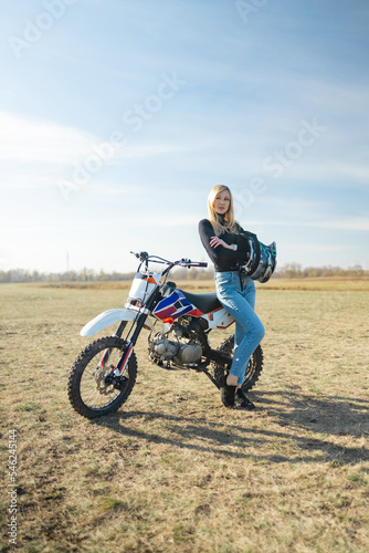Fototapeta Naklejka Na Ścianę i Meble -  Attractive blonde girl on motocross. Sporty woman biker at motobike. Countryside, country road. sunset, female motorcycle rider, motorbike rider travel the world, girl resting, freedom lifestyle