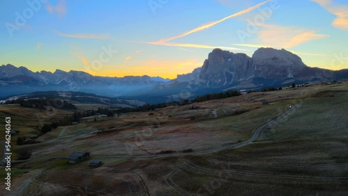 Mountains, forest and grass fields with wooden cabins filmed at Alpe di Siusi in Alps, Italian Dolomites filmed in vibrant colors at sunrise. Filmed with a drone with backwards movement, wide view photo
